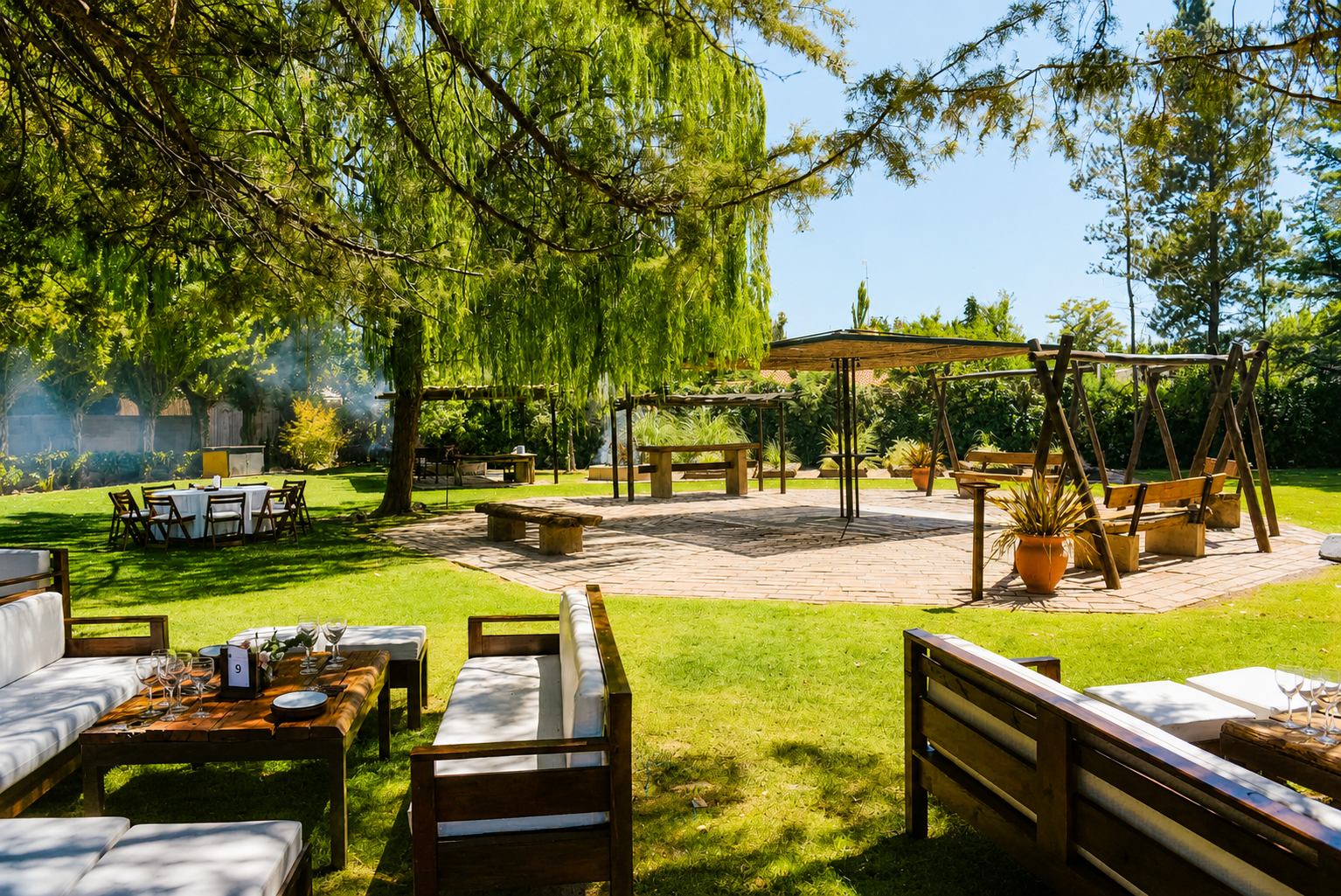 El parque a pleno sol, con los livings y la pérgola de caña bajo los sauces