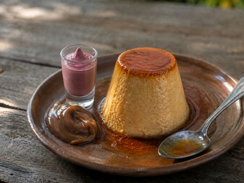 El flan casero con su caramelo y el dulce de leche, con el chupito al lado, en plato de barro